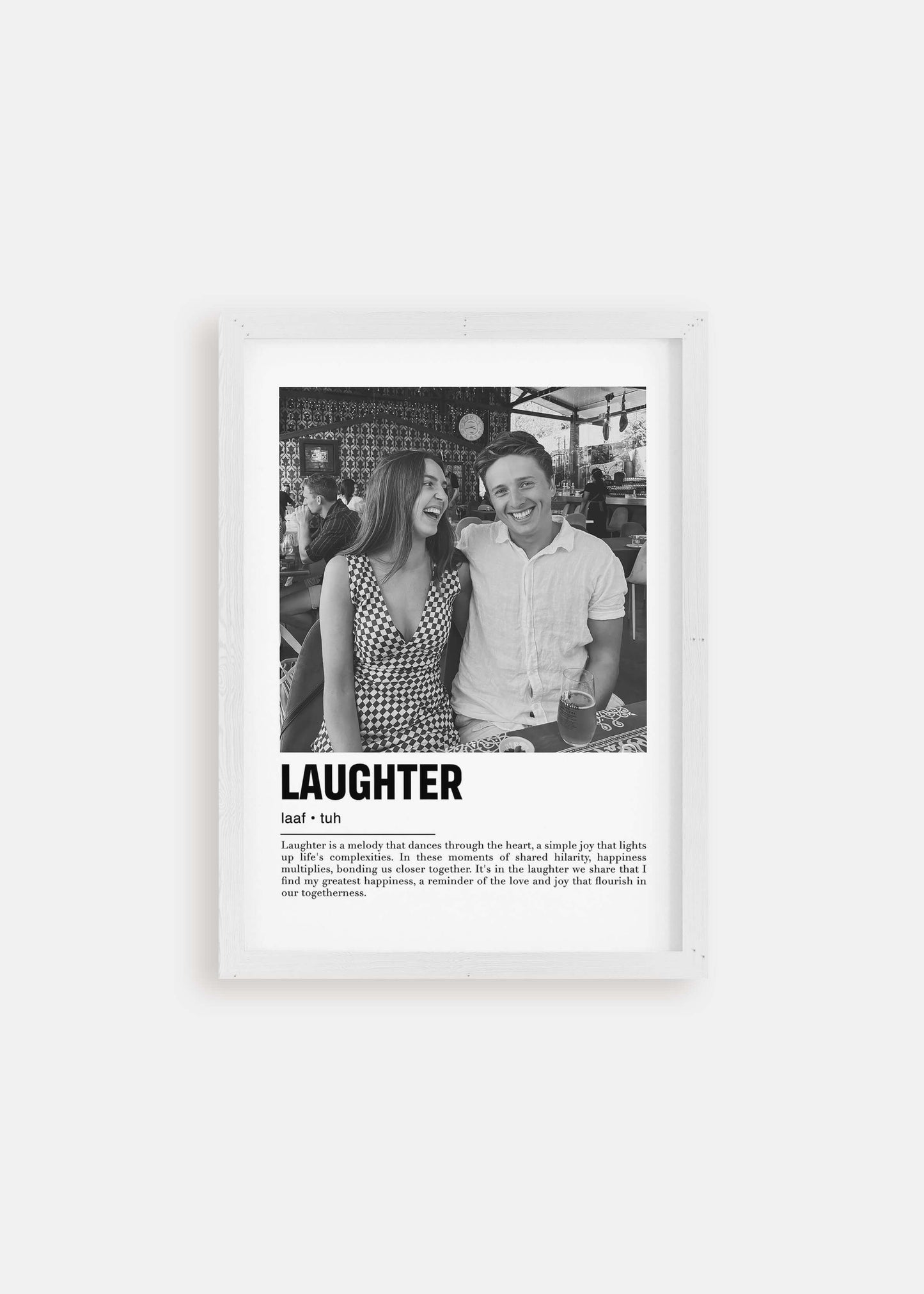 Personalized black and white photo in a white frame of a couple laughing. The custom artwork has a caption that reads Laughter. The white frame is on a white background.