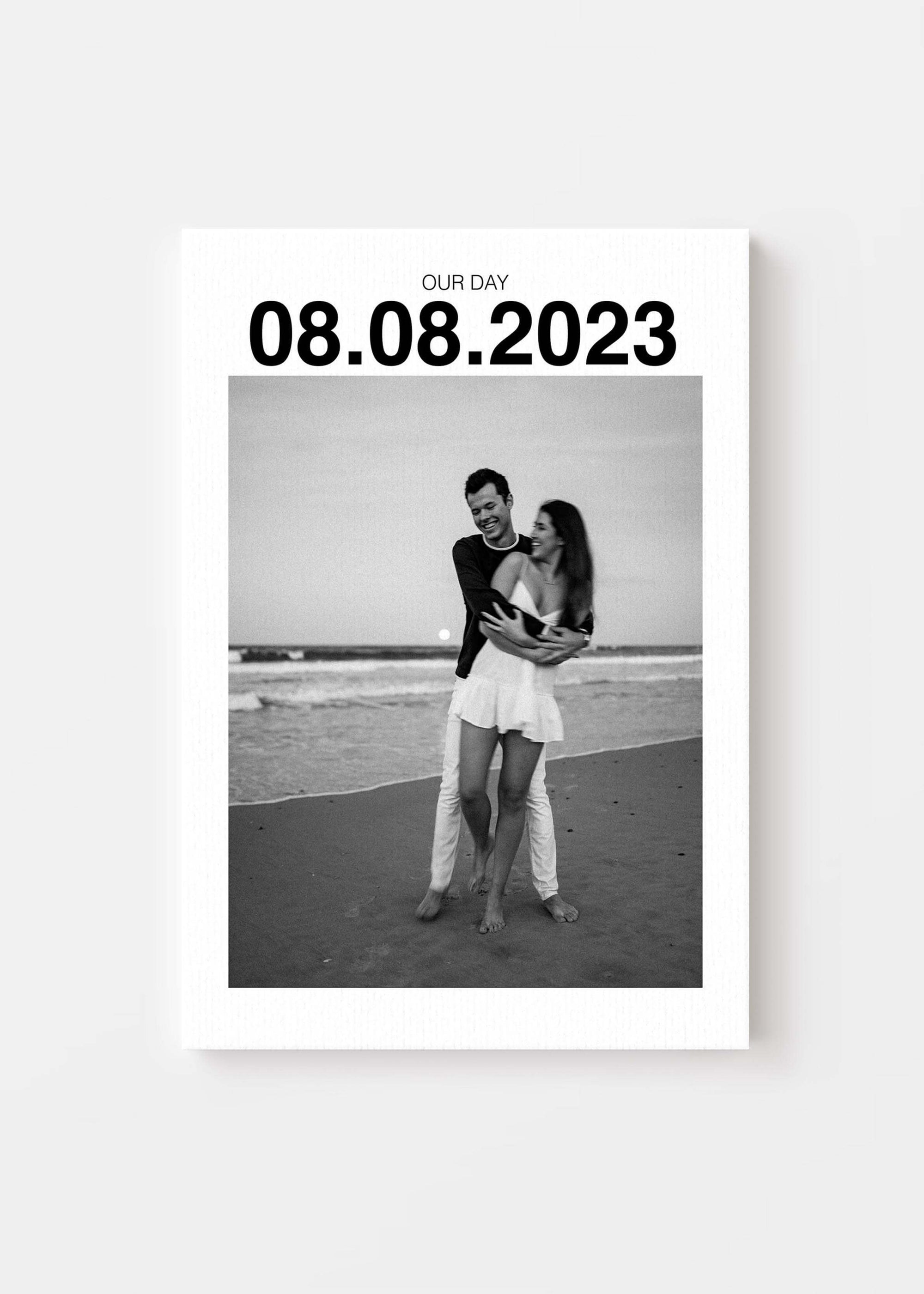 Personalized anniversary gift canvas with large custom date on canvas and a couple on the beach smiling in black and white. Canvas is on a white background.