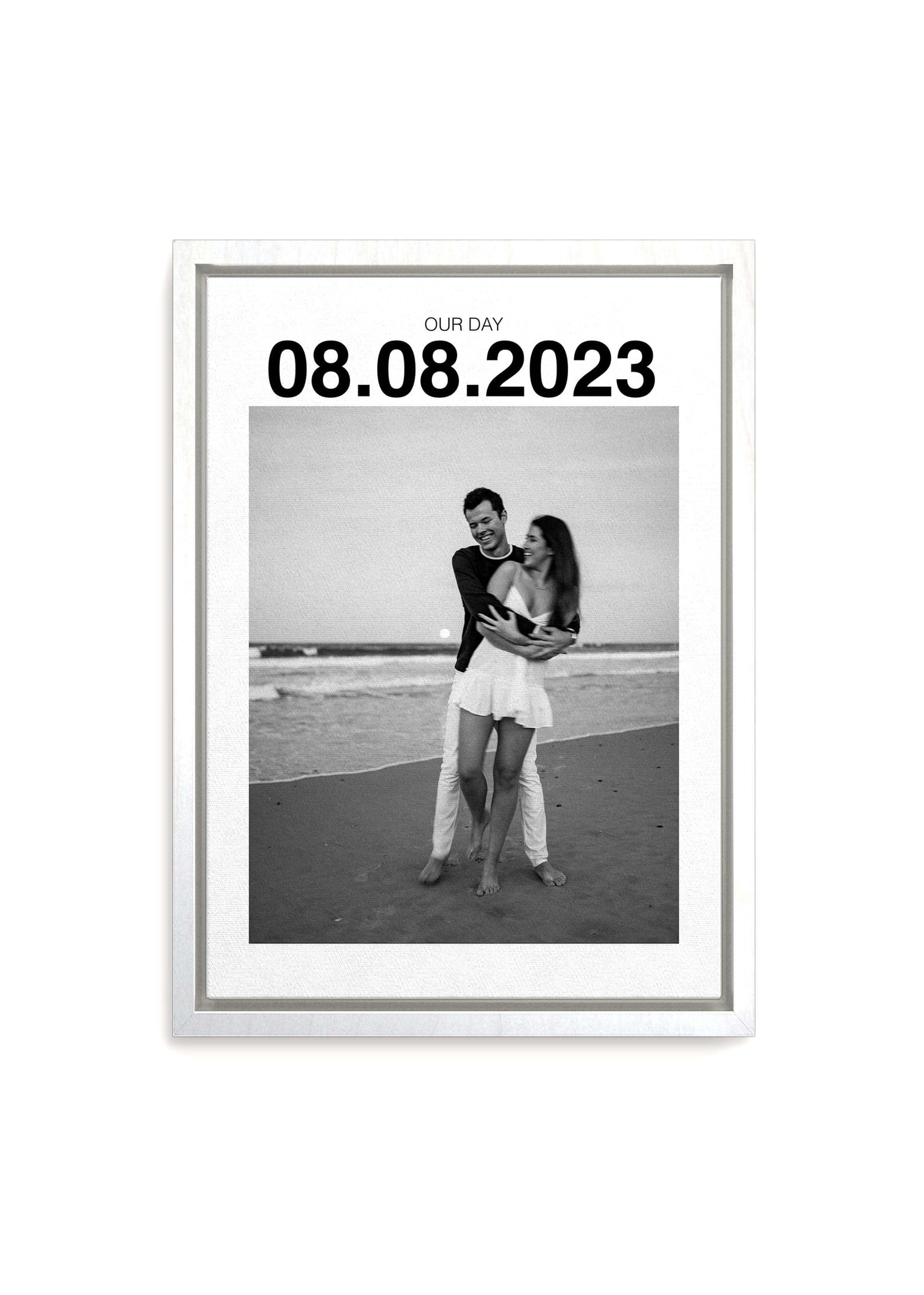 Personalized anniversary gift canvas with large custom date on white framed canvas and a couple on the beach smiling in black and white. Canvas is on a white background.