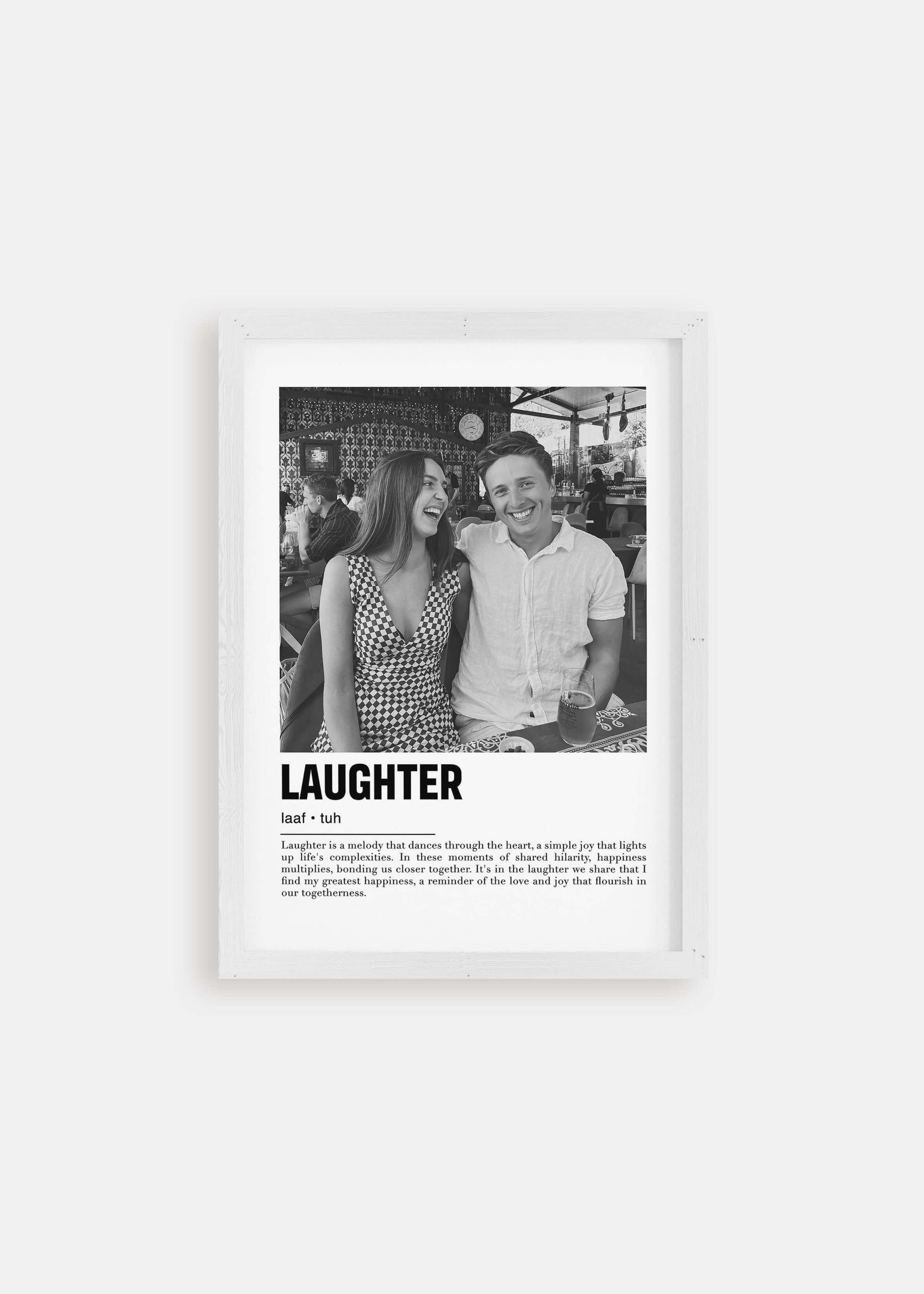 Personalized black and white photo in a white frame of a couple laughing. The custom artwork has a caption that reads Laughter. The white frame is on a white background. 
