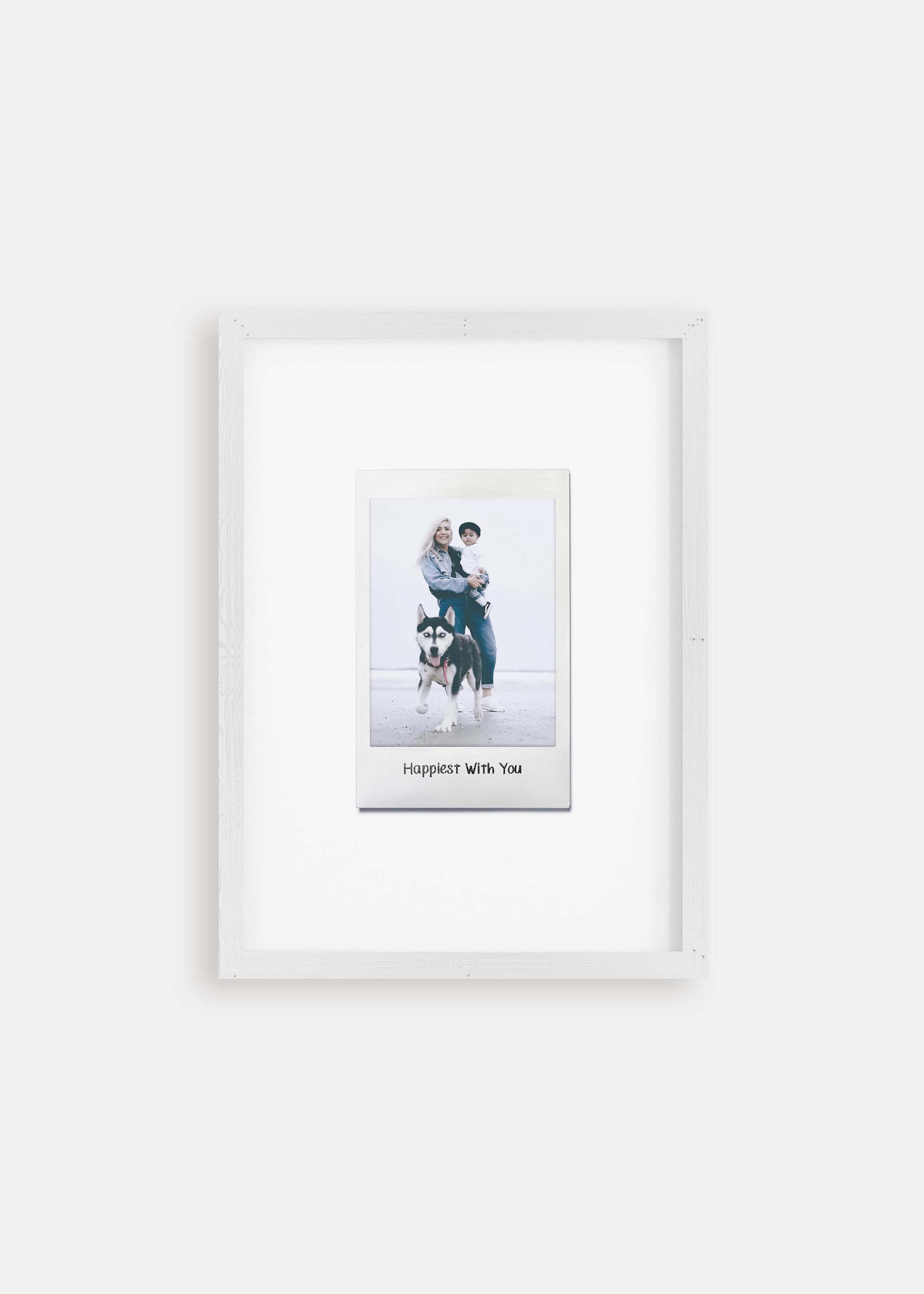 Personalized photo gift of a woman with her child and dog in a white frame in the style of a nostalgic instant film custom polaroid photo with frame on white background. The custom caption reads "Happiest with you".