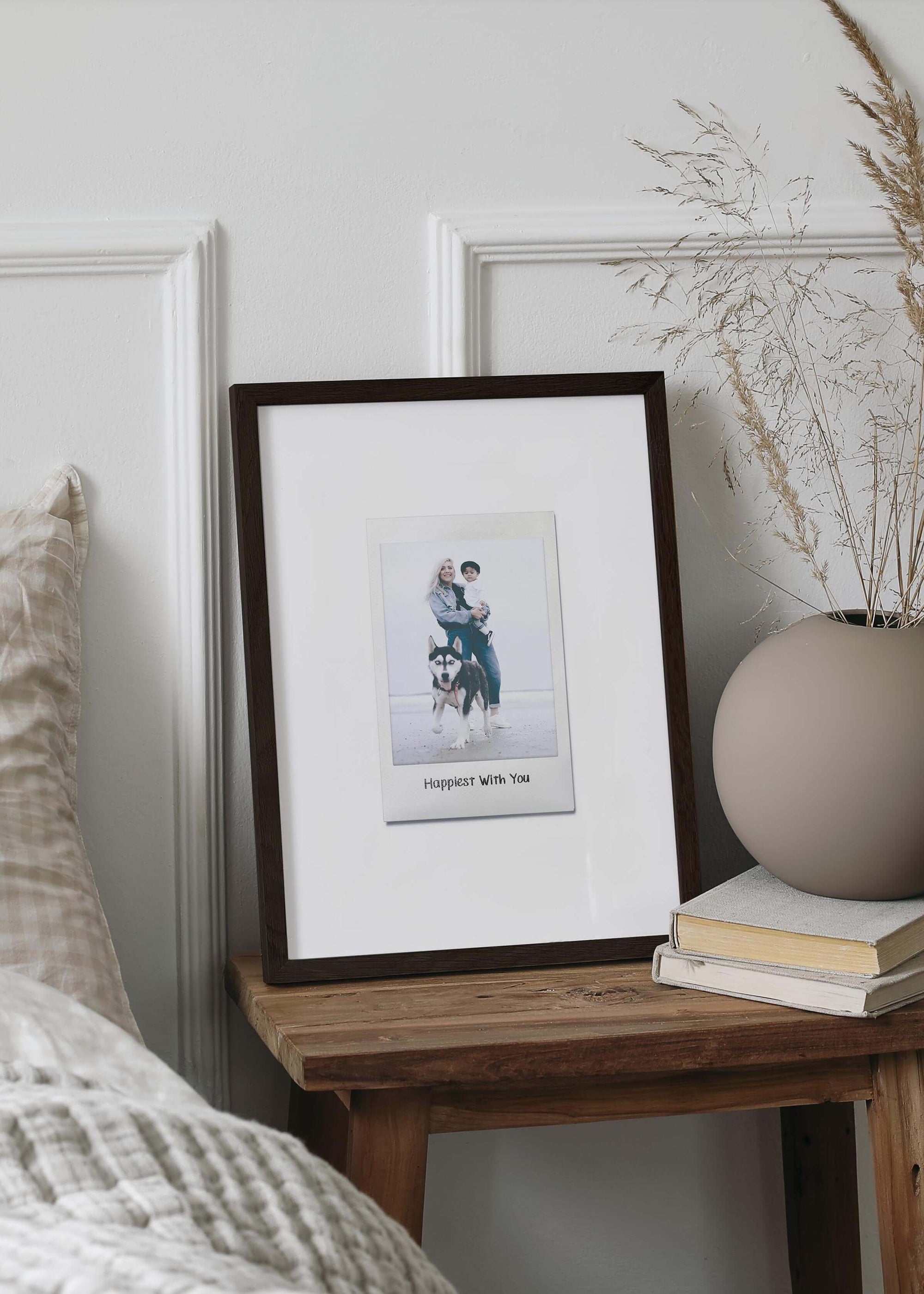 Personalized photo gift of a woman with her child and dog in a walnut frame in the style of a nostalgic instant film custom polaroid photo with frame on a small bedside table. The custom caption reads "Happiest with you".
