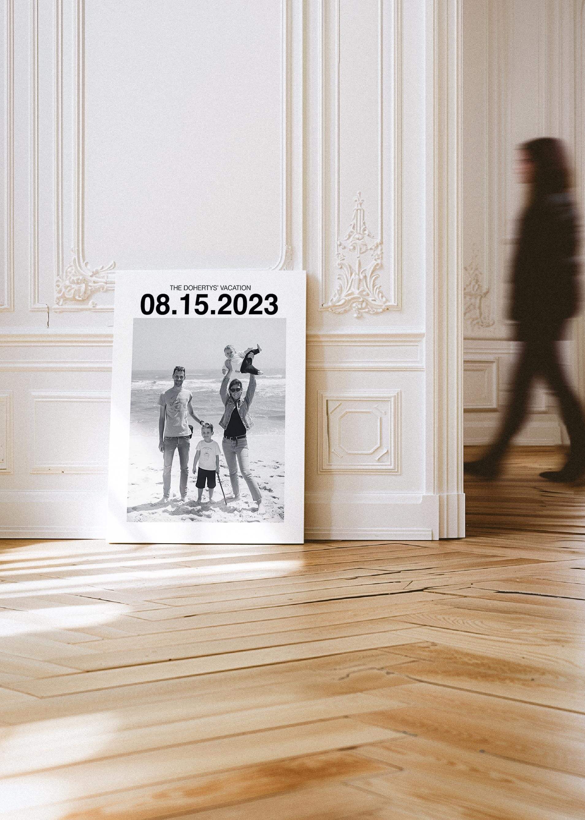 custom personalized black and white photo of a family on holiday. The canvas has a large custom date at the top and the canvas sits against a wall in a contemporary art gallery setting.