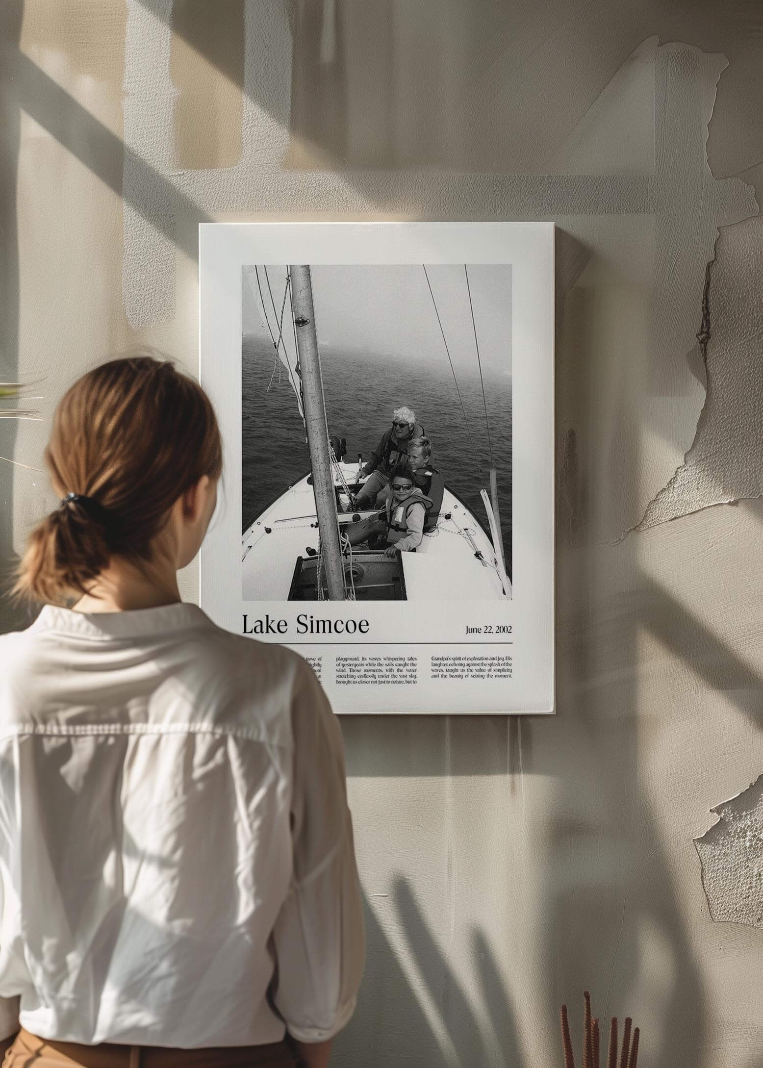 Woman looking at a personalized black and white photo gift on canvas of children with grandpa sailing. The canvas is on a raw concrete wall and has a custom message inscribed on it.