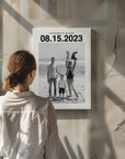 Woman looking at a custom personalized black and white photo of a family on holiday. The canvas has a large custom date at the top and the canvas is mounted on a raw concrete wall.
